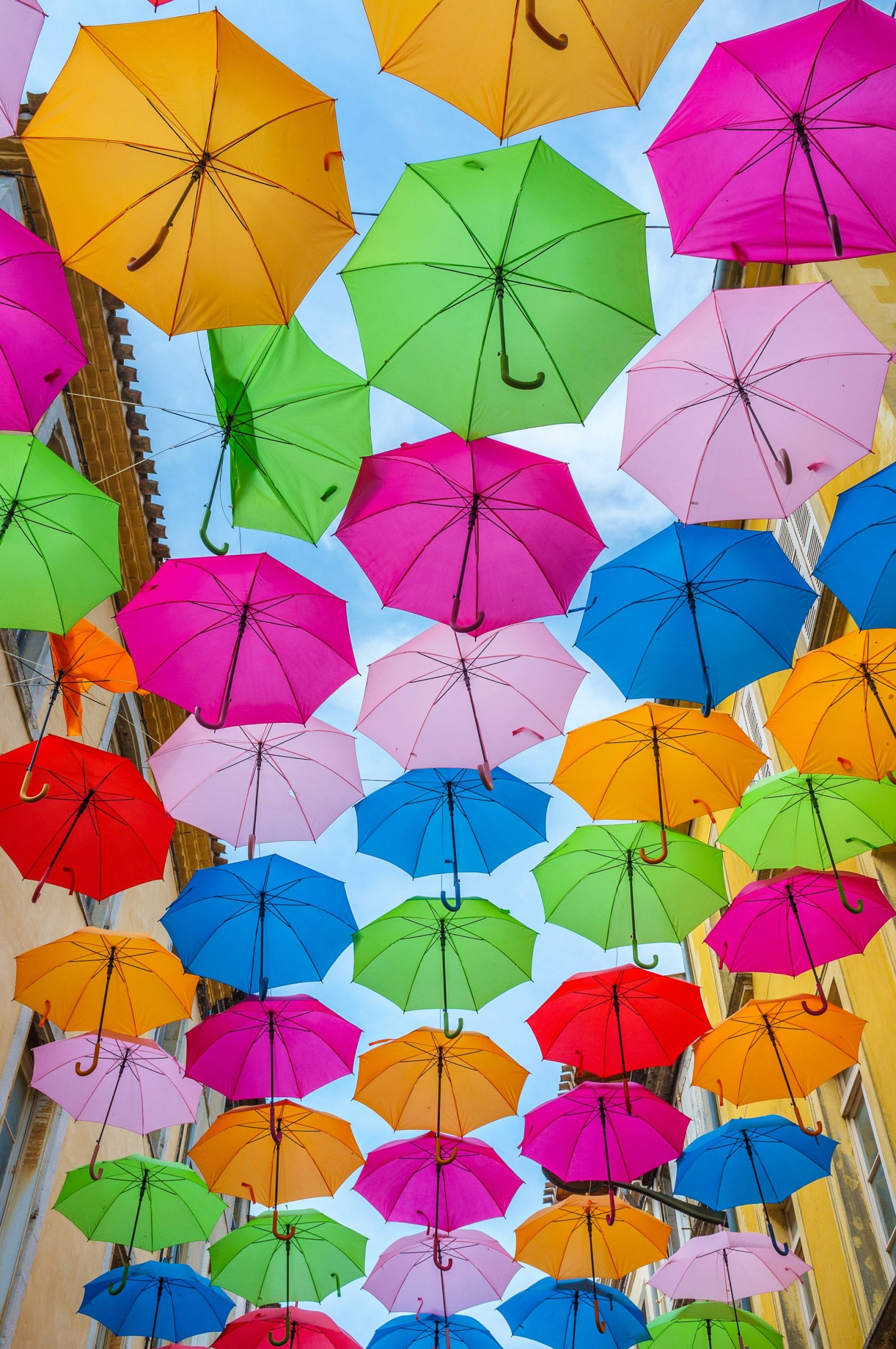 Das Bild zeigt die Fotografie von mehr als zwei Dutzend geöffneten, bunten Regenschirmen. Sie bilden einen bunten Himmel vor einem strahlend blauen Himmel. Es verdeutlicht die große Auswahl an Influencern, während der blaue Himmel dahinter die Realität darstellt.